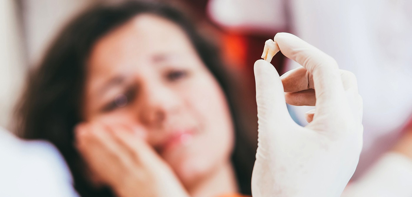 woman looking at extracted tooth being held up